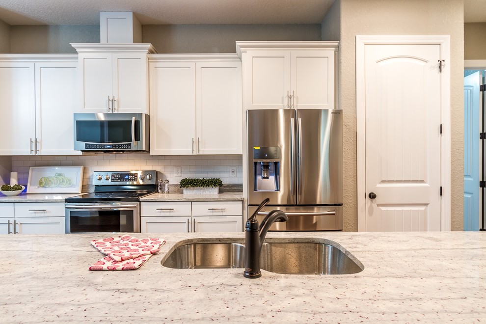Mid-sized transitional l-shaped open plan kitchen in Tampa with a double-bowl sink, shaker cabinets, white cabinets, quartz benchtops, white splashback, subway tile splashback, stainless steel appliances, with island and dark hardwood floors.