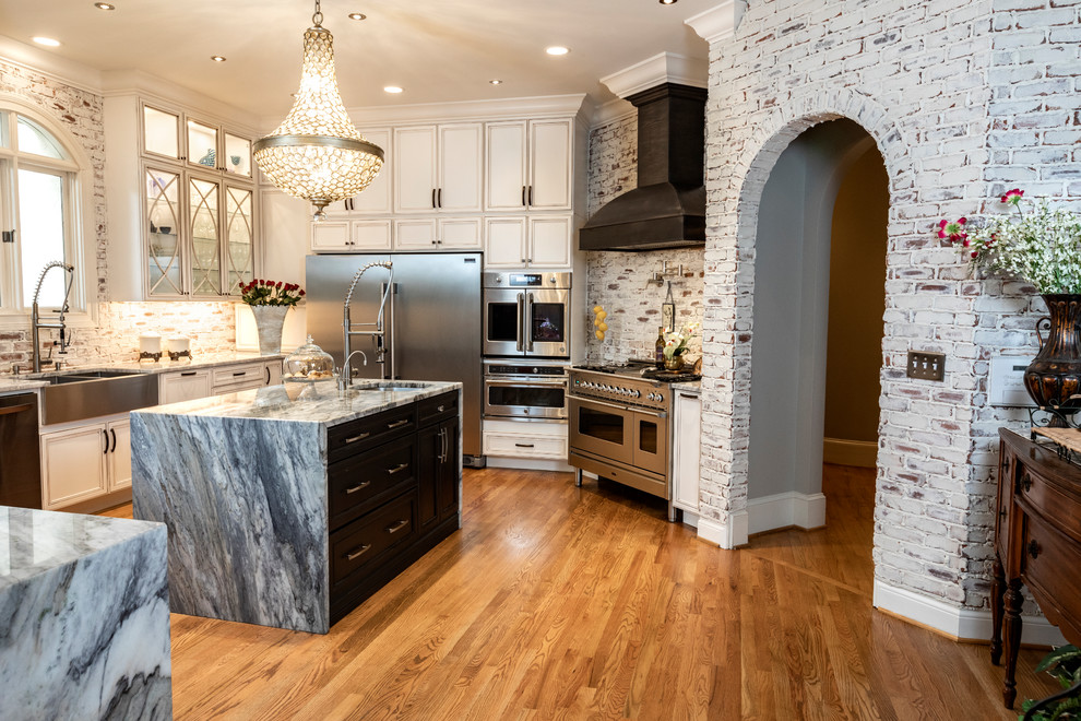 This is an example of a large traditional open plan kitchen in Atlanta with a farmhouse sink, flat-panel cabinets, white cabinets, limestone benchtops, red splashback, brick splashback, stainless steel appliances, light hardwood floors, multiple islands, brown floor and grey benchtop.