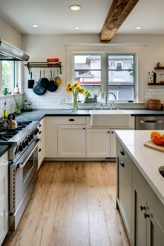 Photo of a mid-sized country l-shaped open plan kitchen in San Francisco with a farmhouse sink, shaker cabinets, white cabinets, white splashback, subway tile splashback, stainless steel appliances, with island, dark hardwood floors, soapstone benchtops and brown floor.