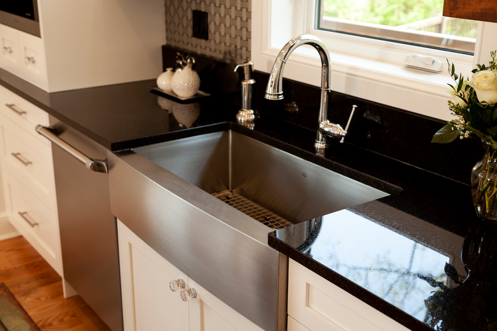 Inspiration for a mid-sized transitional l-shaped enclosed kitchen remodel with a farmhouse sink, shaker cabinets, white cabinets, stainless steel appliances, an island and black countertops