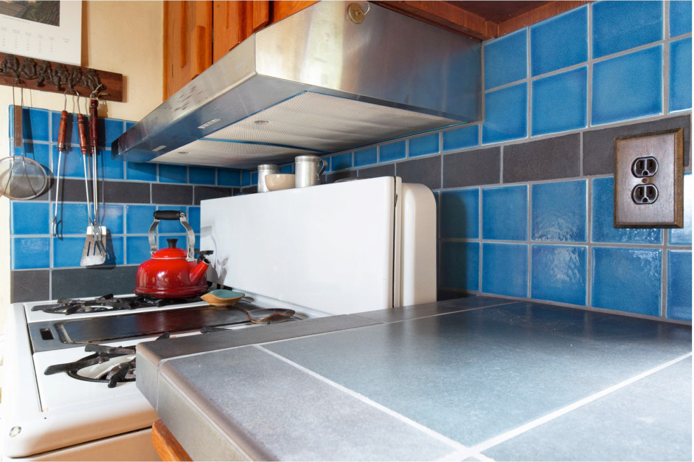 This is an example of a mid-sized country galley open plan kitchen in Other with a double-bowl sink, shaker cabinets, medium wood cabinets, tile benchtops, blue splashback, ceramic splashback, medium hardwood floors, with island and black benchtop.