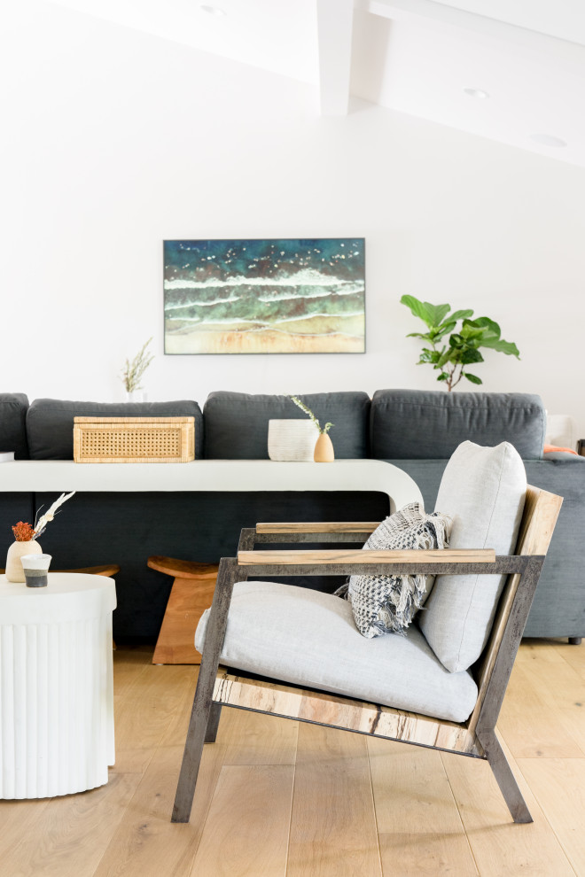 Modelo de sala de estar abierta, abovedada y blanca nórdica de tamaño medio con paredes blancas, suelo de madera clara, televisor colgado en la pared y suelo marrón