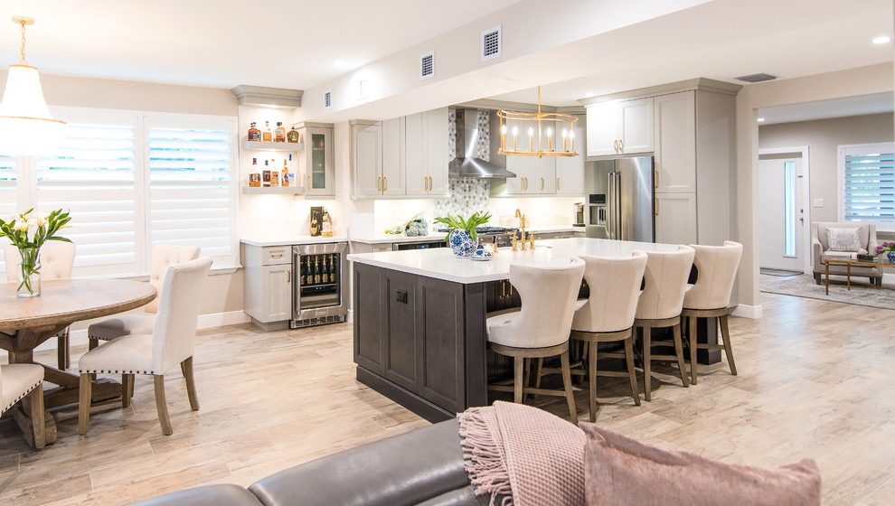 This is an example of a mid-sized country l-shaped open plan kitchen in Miami with a farmhouse sink, recessed-panel cabinets, grey cabinets, quartz benchtops, multi-coloured splashback, porcelain splashback, stainless steel appliances, laminate floors, with island, brown floor and white benchtop.