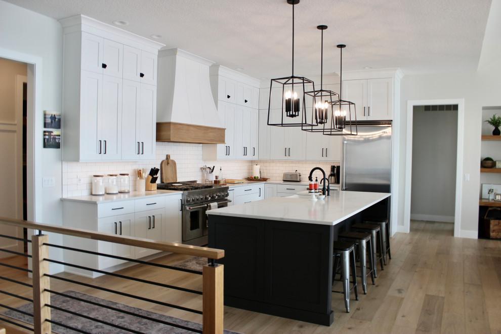 Large transitional l-shaped light wood floor, brown floor and tray ceiling open concept kitchen photo in Other with a farmhouse sink, flat-panel cabinets, white cabinets, quartz countertops, white backsplash, porcelain backsplash, stainless steel appliances, an island and white countertops