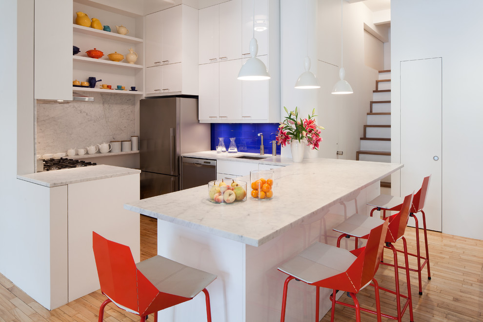 Photo of a contemporary u-shaped kitchen in New York with an undermount sink, flat-panel cabinets, white cabinets, blue splashback, stainless steel appliances, light hardwood floors and a peninsula.