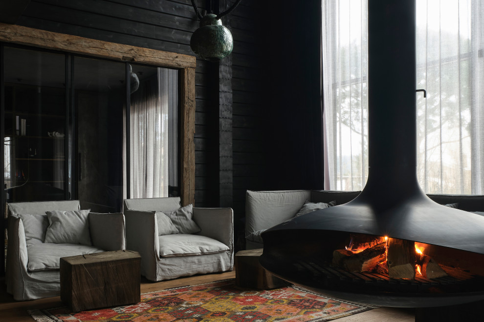 Cette photo montre un salon en bois de taille moyenne avec une bibliothèque ou un coin lecture, un mur noir, cheminée suspendue et un manteau de cheminée en métal.