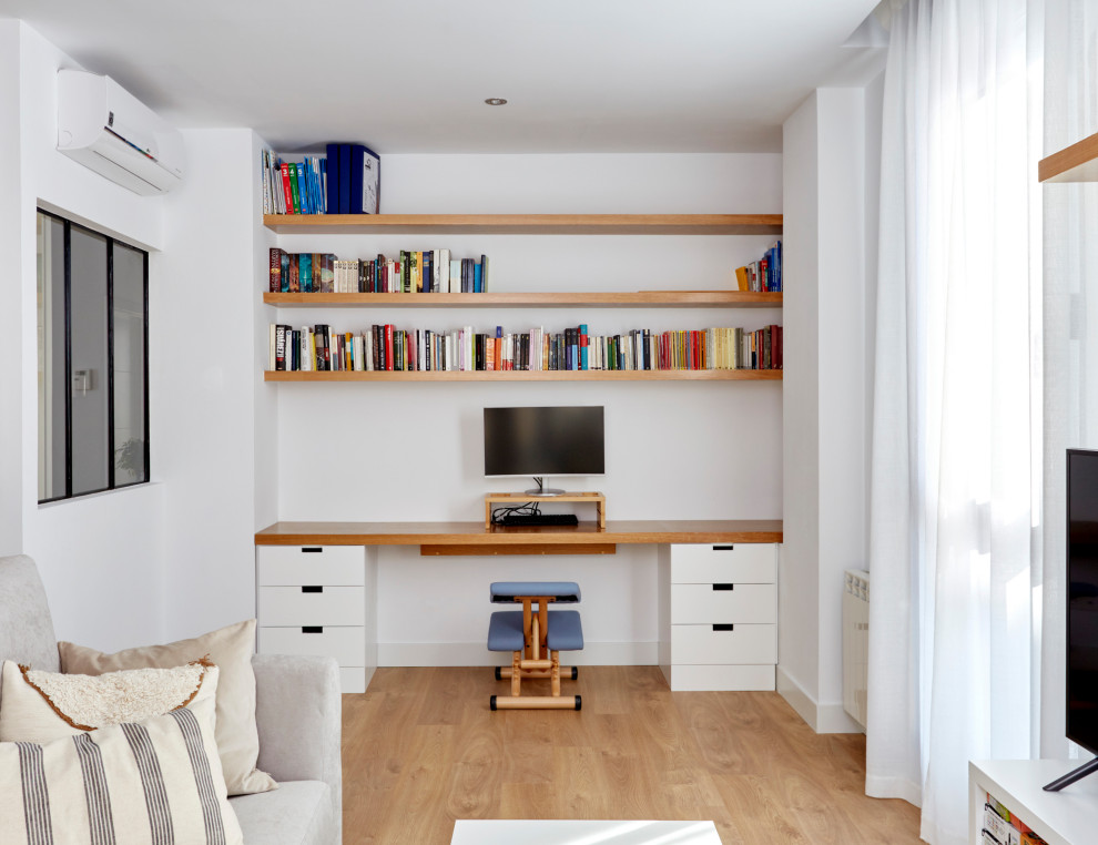 Design ideas for a mid-sized modern home studio in Madrid with white walls, light hardwood floors and a built-in desk.