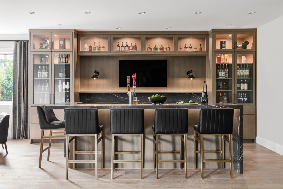 This is an example of a contemporary galley seated home bar in Vancouver with an undermount sink, glass-front cabinets, medium wood cabinets, marble benchtops, multi-coloured splashback, marble splashback, medium hardwood floors, brown floor and multi-coloured benchtop.