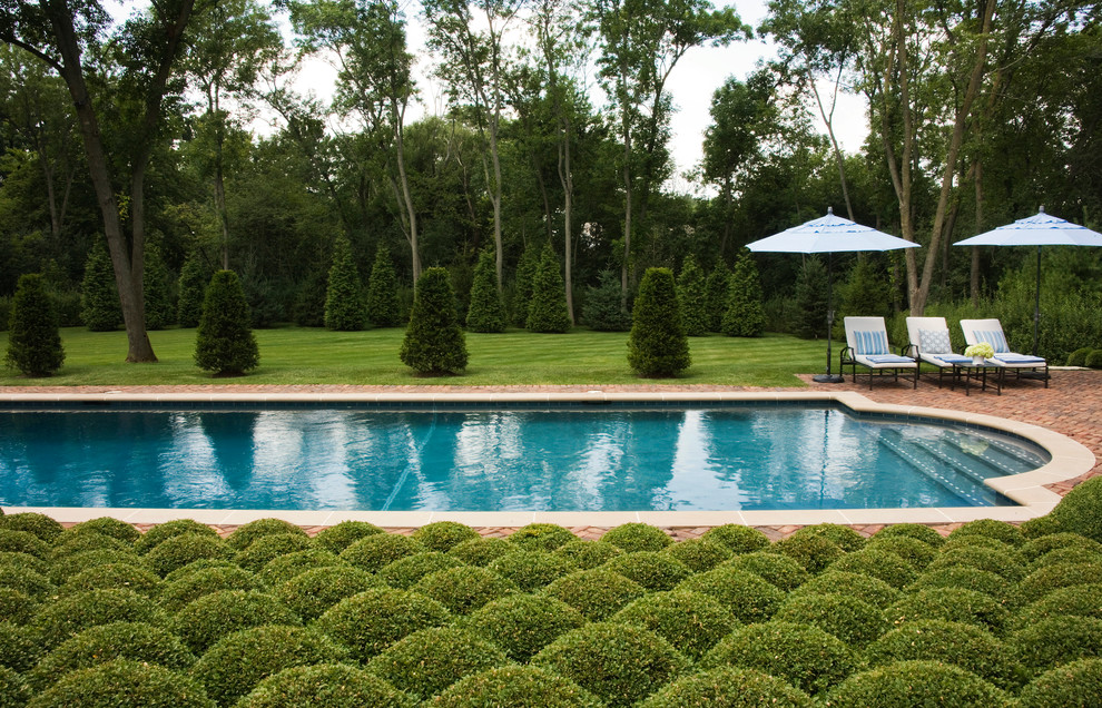 This is an example of an expansive traditional backyard rectangular pool in Chicago with brick pavers and a pool house.