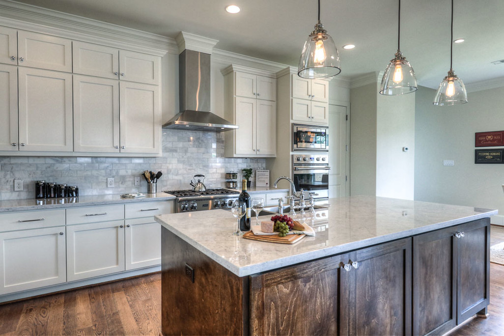 Photo of a mid-sized transitional l-shaped open plan kitchen in Houston with a farmhouse sink, shaker cabinets, white cabinets, marble benchtops, grey splashback, marble splashback, stainless steel appliances, medium hardwood floors, with island, brown floor and grey benchtop.