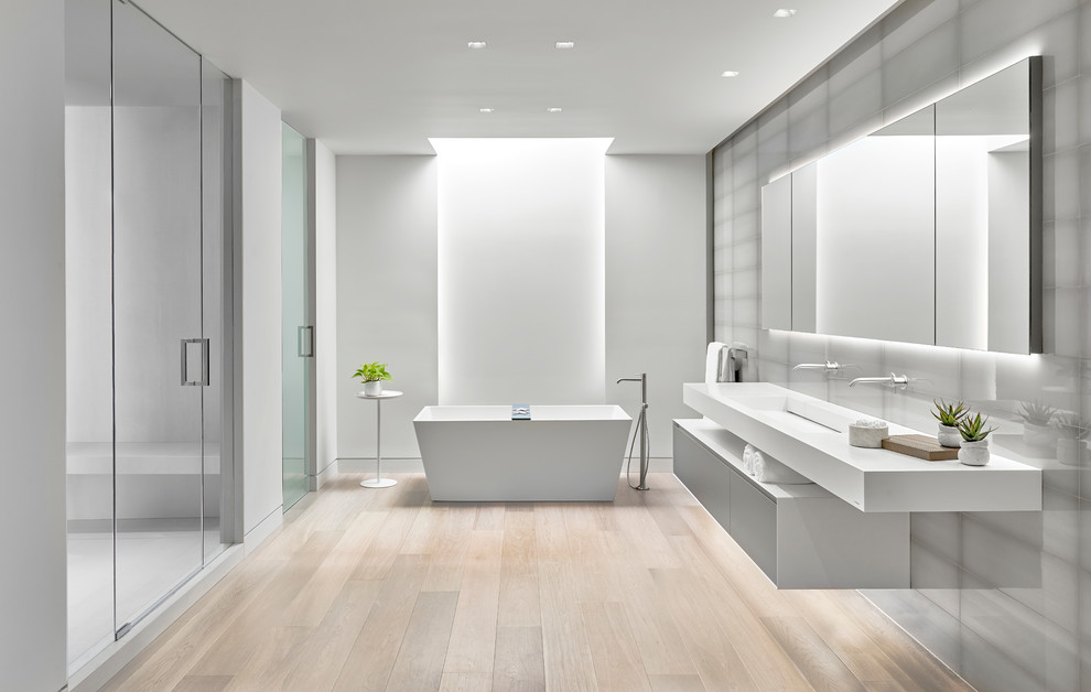 Photo of a large contemporary master wet room bathroom in Chicago with flat-panel cabinets, grey cabinets, a freestanding tub, gray tile, porcelain tile, grey walls, light hardwood floors, a wall-mount sink, solid surface benchtops and a hinged shower door.
