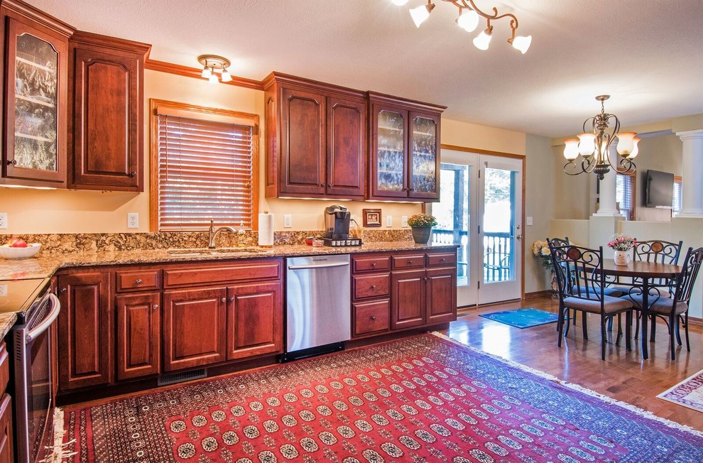 Mid-sized traditional l-shaped kitchen pantry in Cincinnati with an undermount sink, raised-panel cabinets, dark wood cabinets, granite benchtops, stainless steel appliances, medium hardwood floors, no island, brown floor and brown benchtop.
