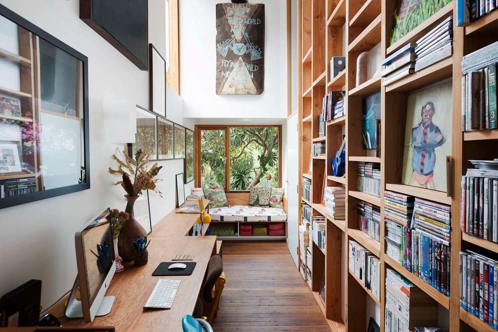 This is an example of an eclectic home office in Sydney with white walls, medium hardwood floors, a built-in desk and a library.