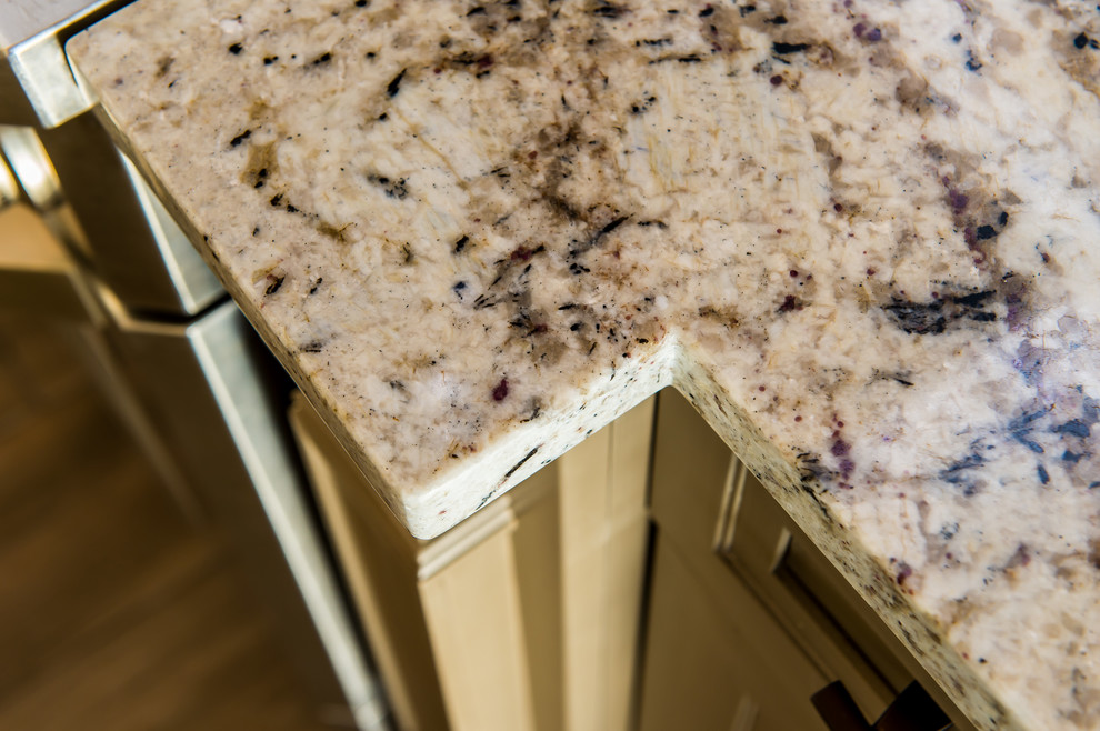 Example of a mid-sized transitional l-shaped porcelain tile eat-in kitchen design in Charleston with a farmhouse sink, shaker cabinets, beige cabinets, granite countertops, brown backsplash, glass tile backsplash, stainless steel appliances and a peninsula