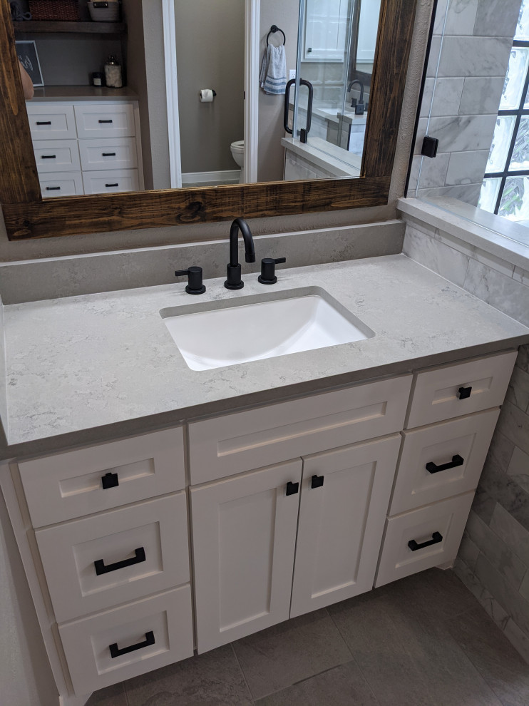 Photo of a transitional master bathroom in Houston with shaker cabinets, white cabinets, a corner shower, a one-piece toilet, white tile, porcelain floors, an undermount sink, engineered quartz benchtops, a hinged shower door, grey benchtops, a shower seat, a double vanity and a built-in vanity.