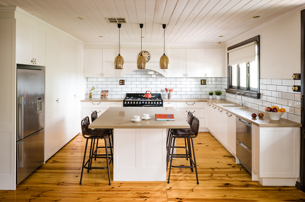 This is an example of a large country u-shaped eat-in kitchen in Melbourne with with island, an undermount sink, white cabinets, white splashback, subway tile splashback, stainless steel appliances, light hardwood floors, shaker cabinets and quartz benchtops.