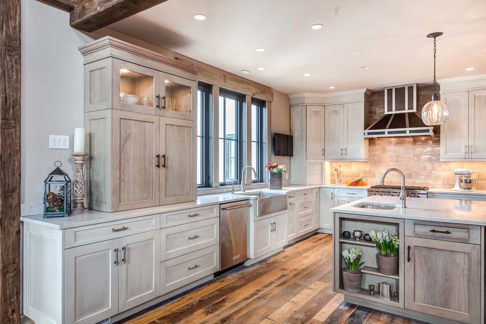 Example of a mountain style l-shaped dark wood floor and brown floor kitchen design in New York with a farmhouse sink, shaker cabinets, light wood cabinets, gray backsplash, stainless steel appliances and an island