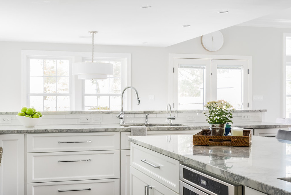 Photo of a mid-sized traditional u-shaped open plan kitchen in Boston with an undermount sink, shaker cabinets, white cabinets, white splashback, subway tile splashback, stainless steel appliances, dark hardwood floors, with island, brown floor, marble benchtops and grey benchtop.