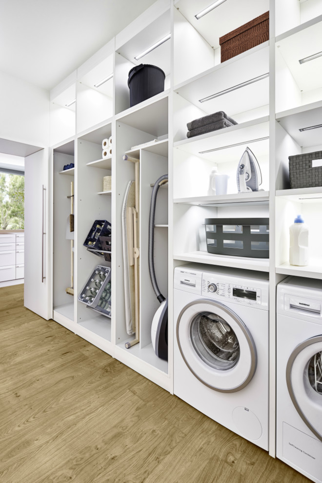 This is an example of a large contemporary single-wall laundry room in Barcelona with flat-panel cabinets, white cabinets, light hardwood floors and brown floor.