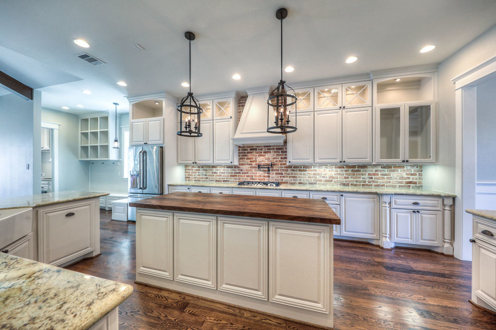 Design ideas for a large arts and crafts galley open plan kitchen in Houston with a farmhouse sink, raised-panel cabinets, white cabinets, wood benchtops, red splashback, stone tile splashback, stainless steel appliances, dark hardwood floors and with island.