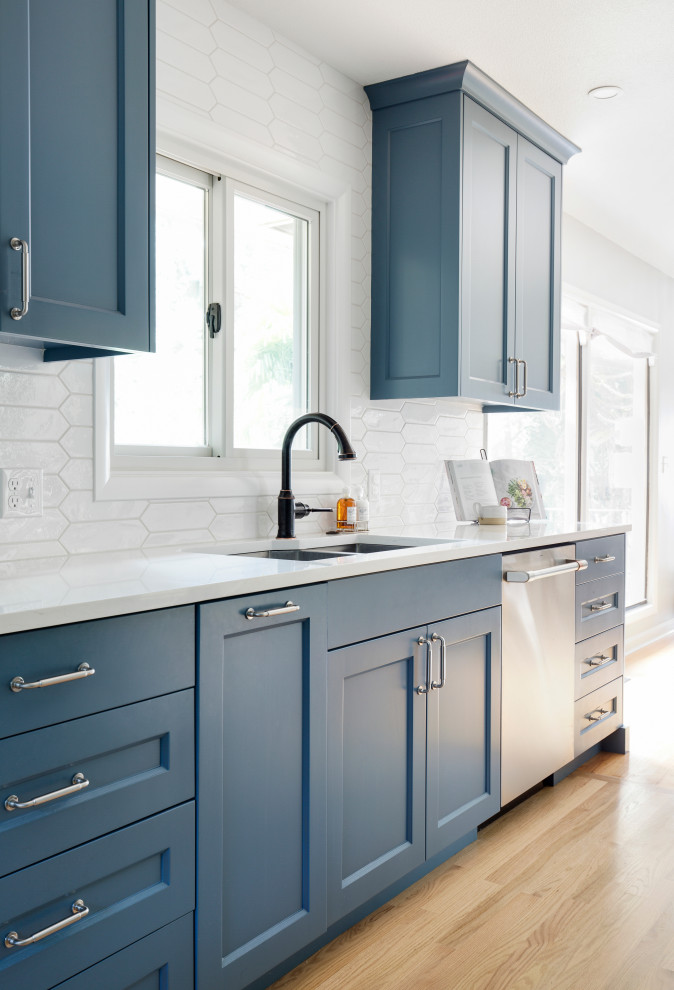 This is an example of a mid-sized transitional galley eat-in kitchen in Portland with an undermount sink, recessed-panel cabinets, blue cabinets, quartz benchtops, white splashback, cement tile splashback, stainless steel appliances, light hardwood floors, no island and white benchtop.