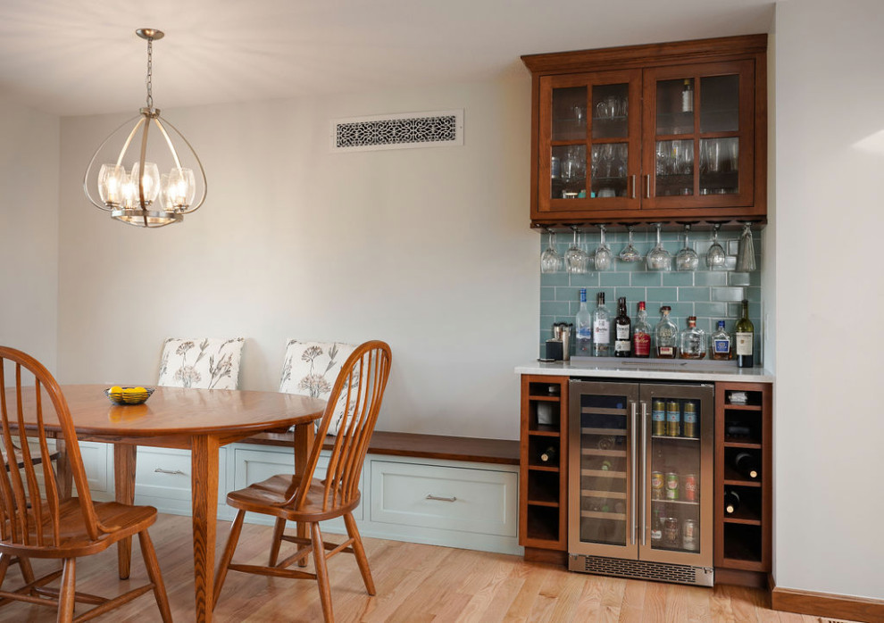 This is an example of a small transitional single-wall home bar in Columbus with glass-front cabinets, brown cabinets, quartz benchtops, blue splashback, ceramic splashback, light hardwood floors, beige floor and white benchtop.