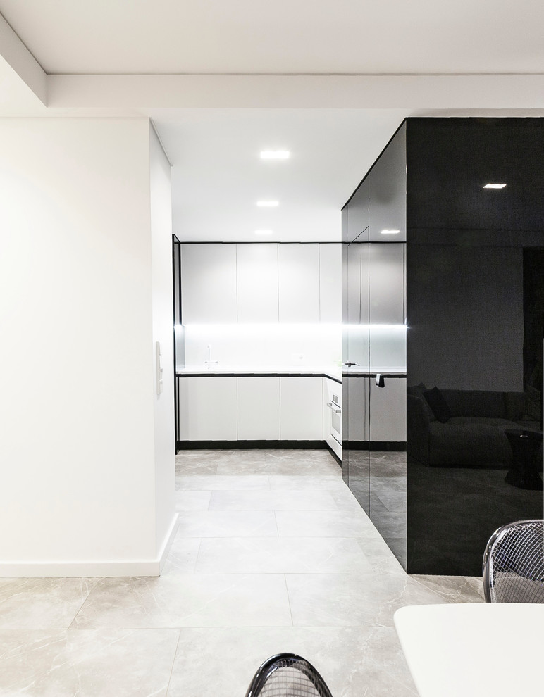 This is an example of a mid-sized contemporary l-shaped separate kitchen in Other with flat-panel cabinets, white cabinets, solid surface benchtops, porcelain splashback, white appliances, porcelain floors, grey floor, white benchtop and white splashback.