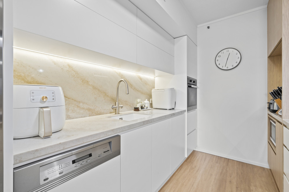 Photo of a large contemporary galley separate kitchen in Gold Coast - Tweed with an undermount sink, flat-panel cabinets, medium wood cabinets, quartz benchtops, beige splashback, engineered quartz splashback, stainless steel appliances, medium hardwood floors, a peninsula and beige benchtop.
