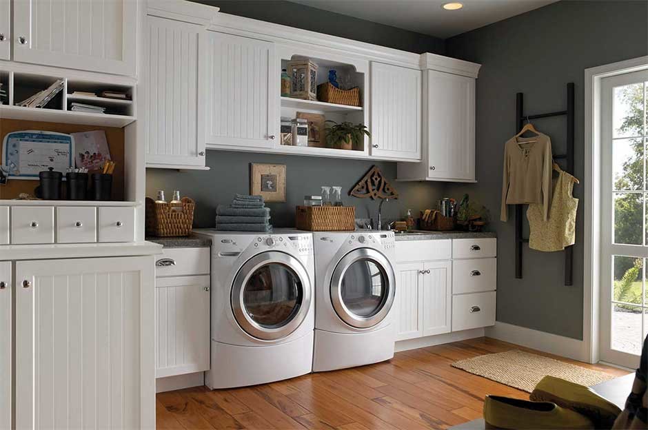 Photo of a mid-sized traditional single-wall utility room in New York with recessed-panel cabinets, white cabinets, granite benchtops, grey walls, medium hardwood floors and a side-by-side washer and dryer.