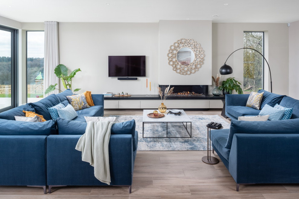 Modelo de sala de estar abierta costera de tamaño medio con paredes blancas, suelo de madera clara, chimenea lineal, televisor independiente y suelo gris