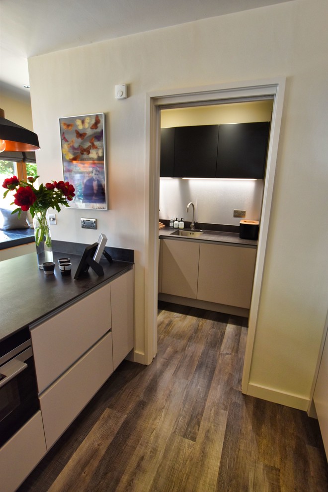 Photo of a large contemporary kitchen/diner in Cambridgeshire with a submerged sink, flat-panel cabinets, beige cabinets, black appliances, light hardwood flooring, an island and grey worktops.