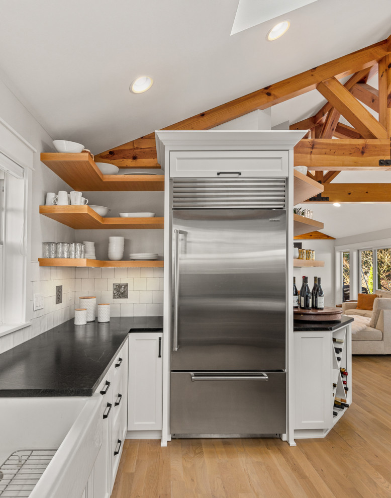 Inspiration for a country eat-in kitchen in Portland with a farmhouse sink, shaker cabinets, white cabinets, soapstone benchtops, white splashback, subway tile splashback, stainless steel appliances, light hardwood floors, with island, black benchtop and vaulted.