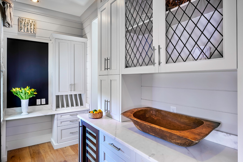 This is an example of a mid-sized traditional l-shaped kitchen pantry in Atlanta with beaded inset cabinets, white cabinets, marble benchtops, white splashback, stainless steel appliances, light hardwood floors, with island, timber splashback and brown floor.