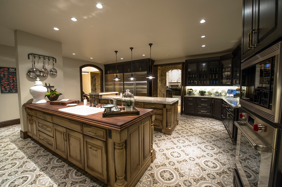 Inspiration for an expansive country u-shaped separate kitchen in Denver with multiple islands, an undermount sink, raised-panel cabinets, distressed cabinets, soapstone benchtops, multi-coloured splashback, mosaic tile splashback, stainless steel appliances, vinyl floors and multi-coloured floor.