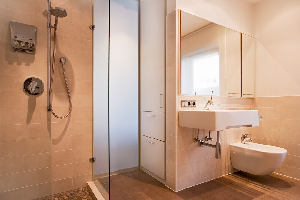Duschbad mit flächenbündigen Schrankfronten, dunklen Holzschränken, bodengleicher Dusche, Bidet, beigen Fliesen, weißer Wandfarbe, Wandwaschbecken, braunem Boden und offener Dusche in Berlin
