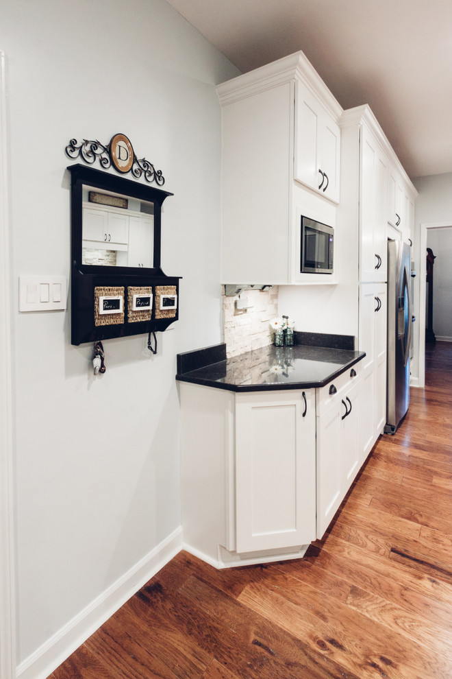 Open concept kitchen - large transitional galley light wood floor and brown floor open concept kitchen idea with an undermount sink, shaker cabinets, white cabinets, quartz countertops, white backsplash, stone tile backsplash, stainless steel appliances and a peninsula