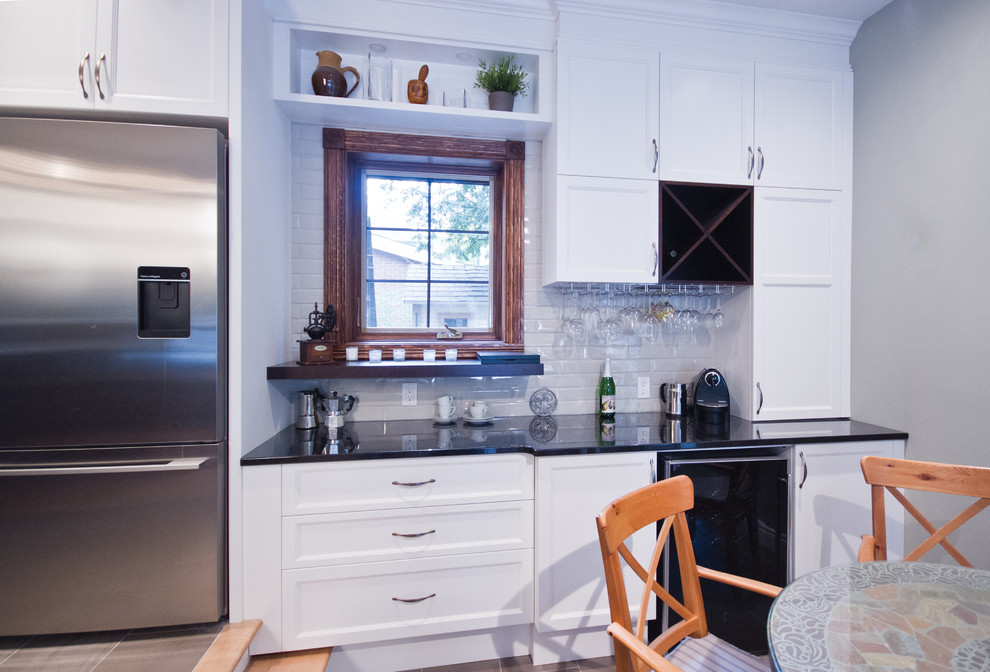 Eat-in kitchen - mid-sized transitional galley ceramic tile eat-in kitchen idea in Montreal with an undermount sink, shaker cabinets, white cabinets, granite countertops, beige backsplash, subway tile backsplash, stainless steel appliances and an island