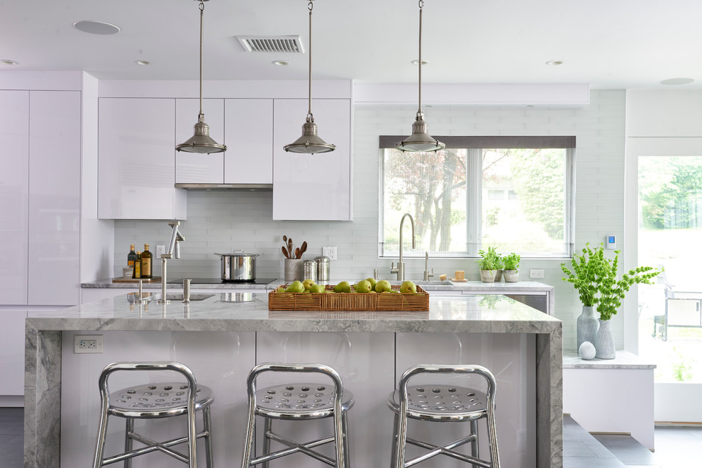 Photo of a large contemporary l-shaped eat-in kitchen in New York with an undermount sink, flat-panel cabinets, white cabinets, white splashback, glass tile splashback, stainless steel appliances, with island and marble benchtops.