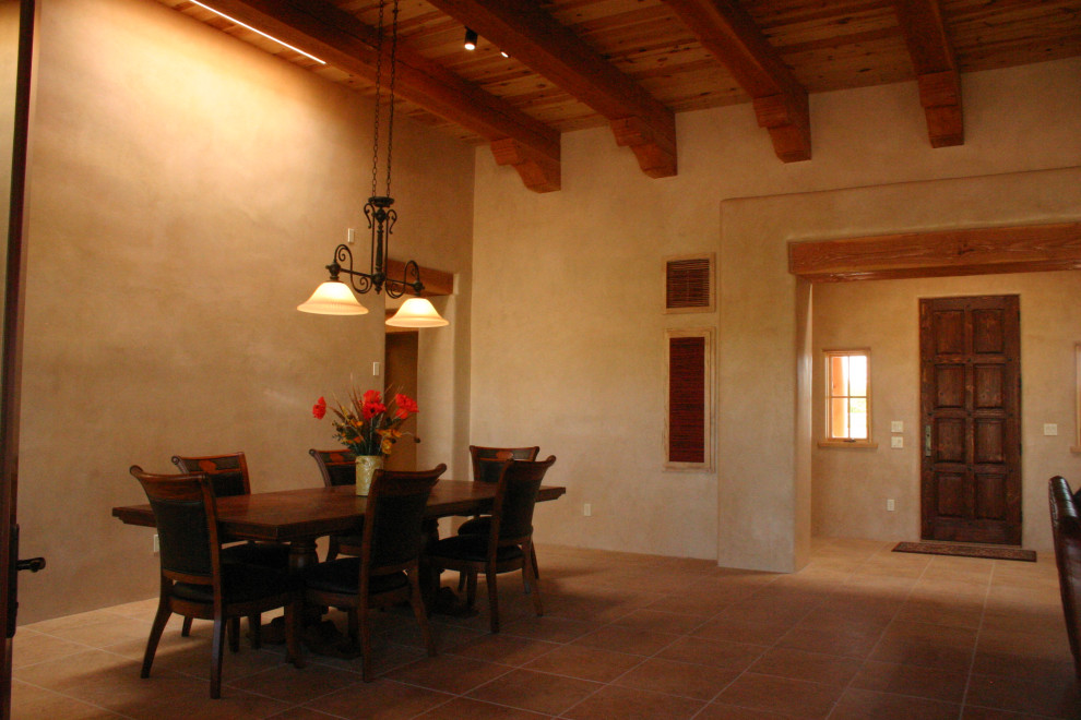 Photo of a large dining room in Albuquerque with beige walls, brick floors, a standard fireplace, a plaster fireplace surround, red floor, exposed beam, vaulted and wood.