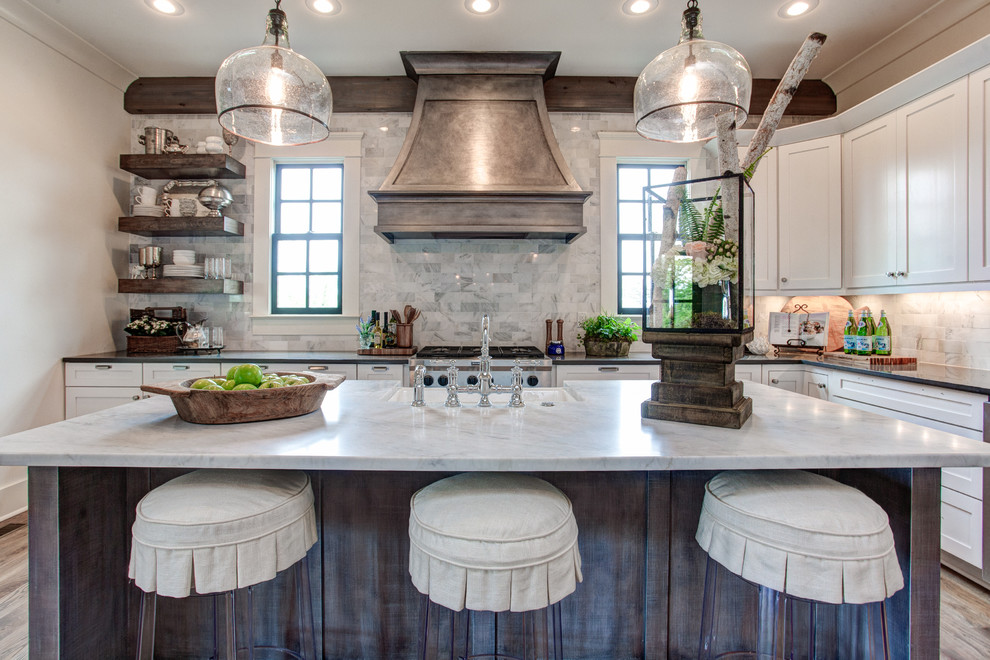 Large transitional l-shaped open plan kitchen in Little Rock with a farmhouse sink, shaker cabinets, white cabinets, grey splashback, stone tile splashback, stainless steel appliances, with island and marble benchtops.