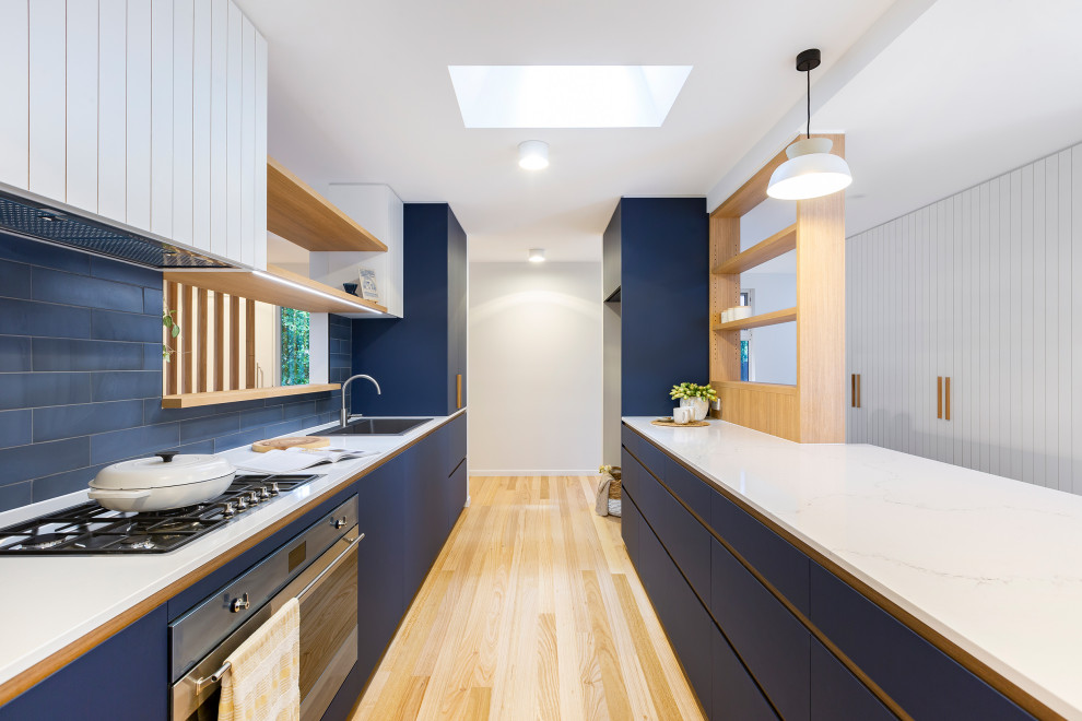Design ideas for a medium sized contemporary galley kitchen pantry in Canberra - Queanbeyan with a built-in sink, blue cabinets, engineered stone countertops, blue splashback, cement tile splashback, stainless steel appliances, medium hardwood flooring and white worktops.