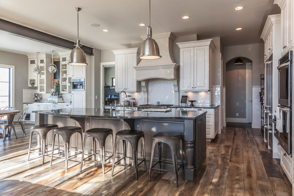 Inspiration for a transitional medium tone wood floor kitchen remodel in Denver with a farmhouse sink, raised-panel cabinets, white cabinets, soapstone countertops, white backsplash, subway tile backsplash, stainless steel appliances and an island