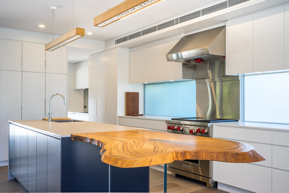 Contemporary galley kitchen in Sydney with an undermount sink, flat-panel cabinets, white cabinets, wood benchtops, stainless steel appliances, bamboo floors, with island and brown benchtop.