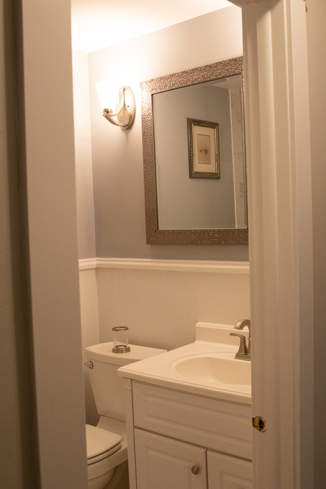 This is an example of a medium sized classic cloakroom in New York with raised-panel cabinets, white cabinets, white tiles, grey walls, mosaic tile flooring, solid surface worktops, multi-coloured floors, white worktops, a freestanding vanity unit and wainscoting.
