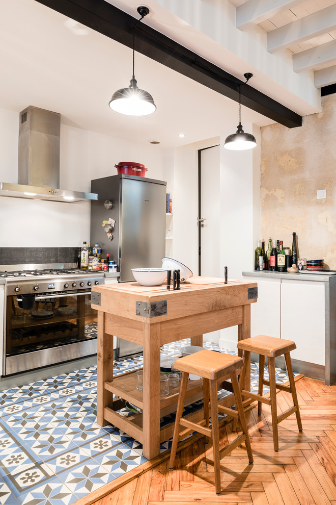 Photo of a mid-sized industrial galley eat-in kitchen in Bordeaux with zinc benchtops, black splashback, stainless steel appliances, ceramic floors, white cabinets and with island.