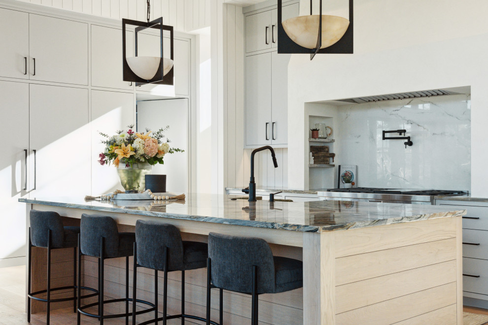 Inspiration for a transitional l-shaped medium tone wood floor and brown floor kitchen remodel in Charleston with a farmhouse sink, flat-panel cabinets, gray cabinets, white backsplash, stone slab backsplash, stainless steel appliances, an island and multicolored countertops