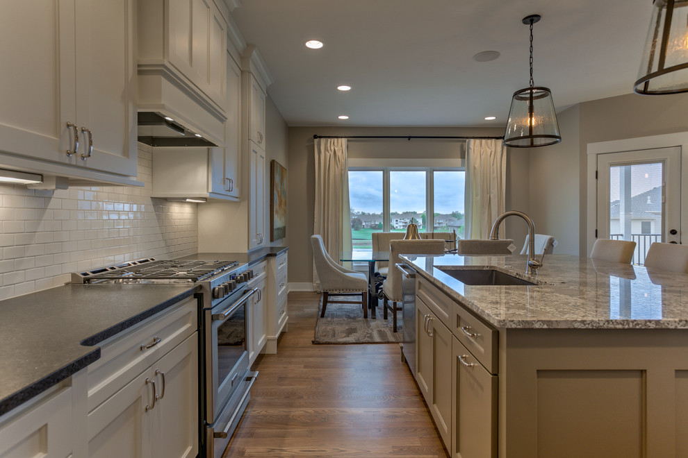 Inspiration for a mid-sized transitional l-shaped medium tone wood floor and beige floor eat-in kitchen remodel in Omaha with an undermount sink, recessed-panel cabinets, white cabinets, granite countertops, white backsplash, subway tile backsplash, stainless steel appliances and an island
