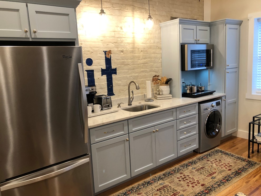 Open concept kitchen - small transitional single-wall light wood floor and brown floor open concept kitchen idea with an undermount sink, recessed-panel cabinets, gray cabinets, marble countertops, white backsplash, brick backsplash, stainless steel appliances, no island and gray countertops