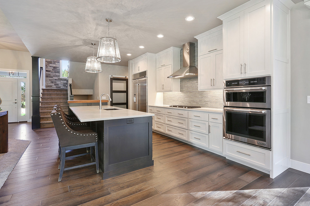 Kitchen pantry - large transitional single-wall dark wood floor and brown floor kitchen pantry idea with an undermount sink, shaker cabinets, white cabinets, quartz countertops, gray backsplash, glass tile backsplash, stainless steel appliances and an island