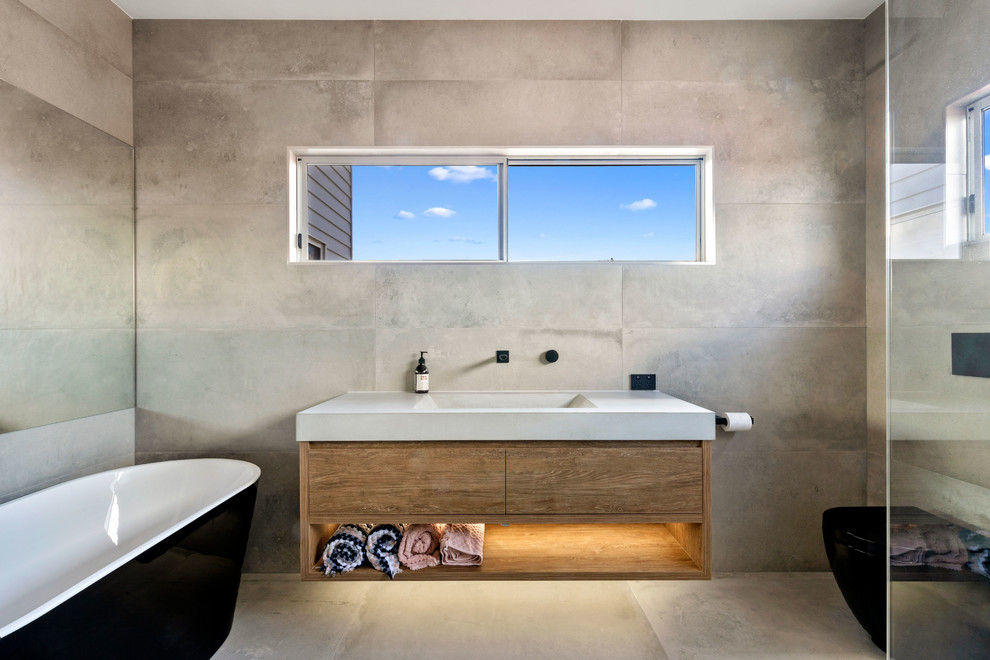 This is an example of a contemporary bathroom in Sunshine Coast with gray tile, a trough sink, concrete benchtops, flat-panel cabinets, medium wood cabinets, a freestanding tub, grey walls, grey floor and grey benchtops.